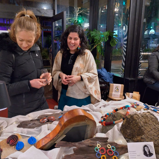 Two female looking at a table with jewellery, displayed on top of rocks. One of them is laughing