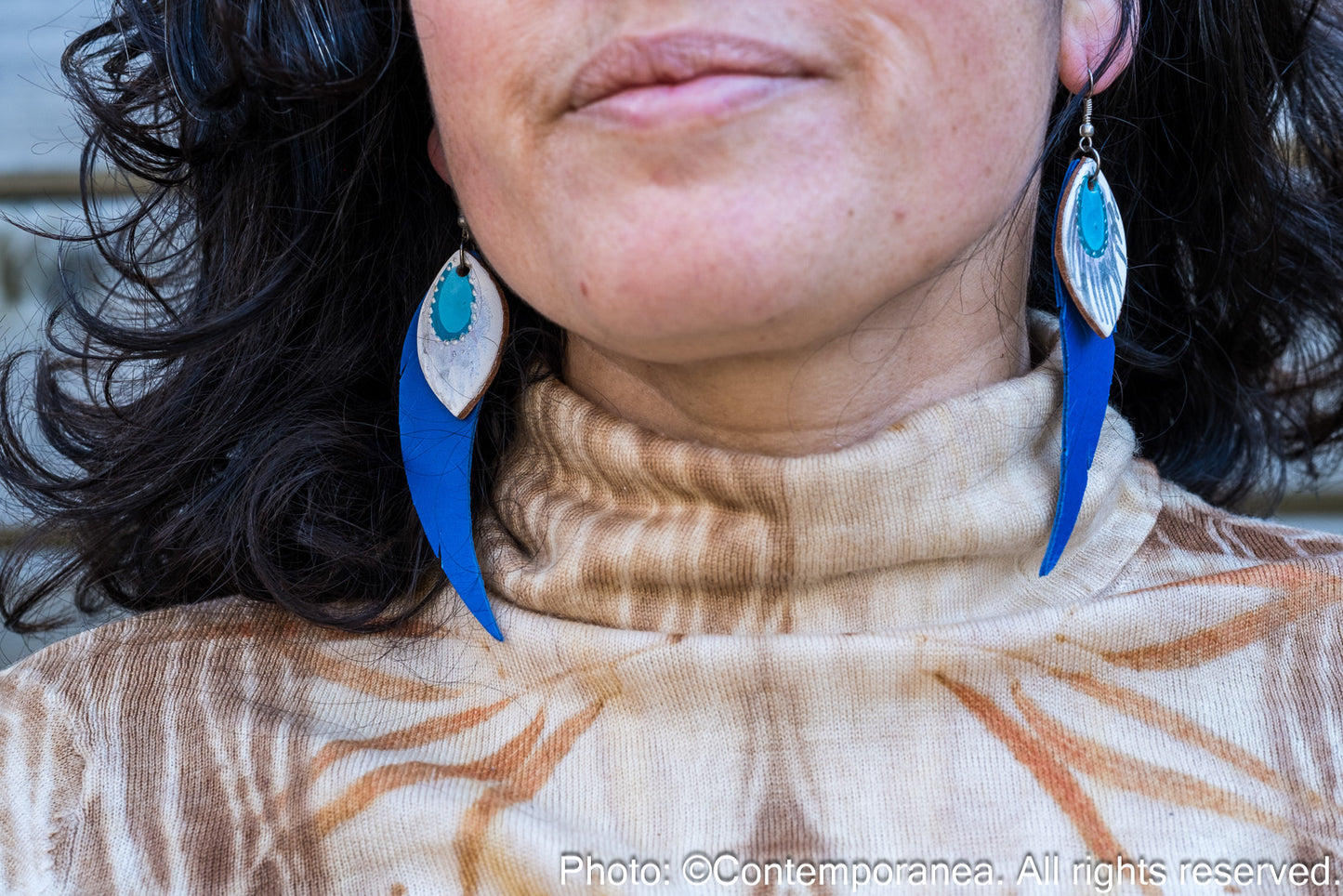 Close-up of a person wearing blue and silver earrings with a blurred background