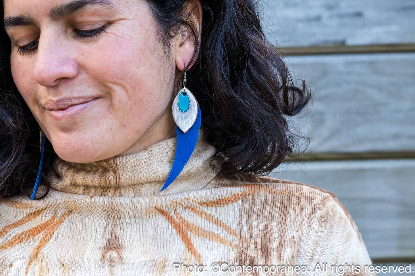 Close-up of a person wearing blue and silver earrings with a blurred background