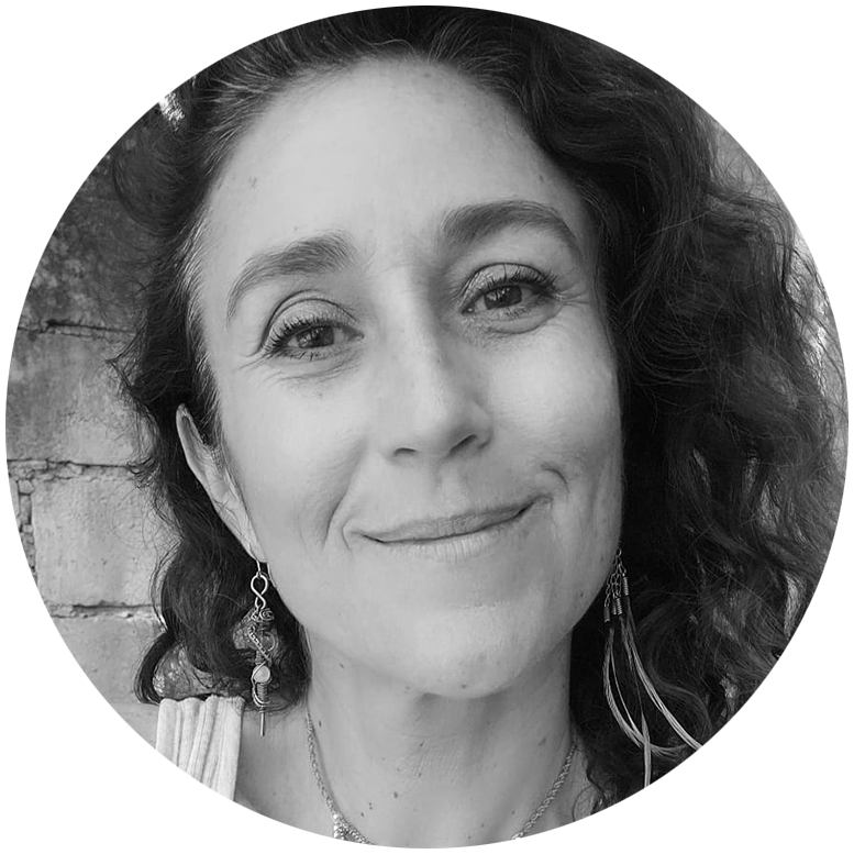 A female person with Latin American features, smiling and faces forward, She is wearing a headband and a necklace with a crystal 