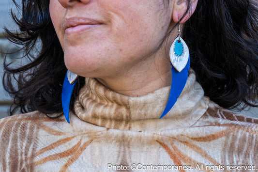 Close-up of a woman wearing a patterned top and feather-shaped blue and silver earrings against a wooden background